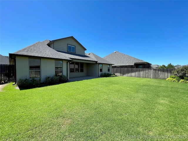 rear view of house featuring brick siding, fence, and a lawn