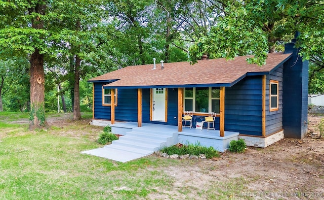 view of front of home with covered porch, a shingled roof, a chimney, and a front lawn