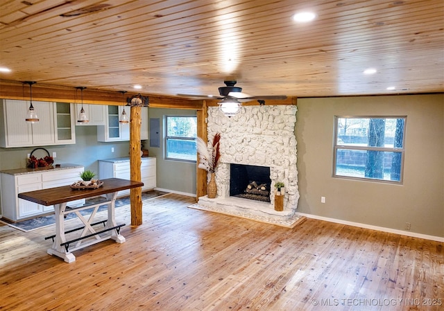 living area featuring a stone fireplace, recessed lighting, baseboards, light wood-type flooring, and electric panel