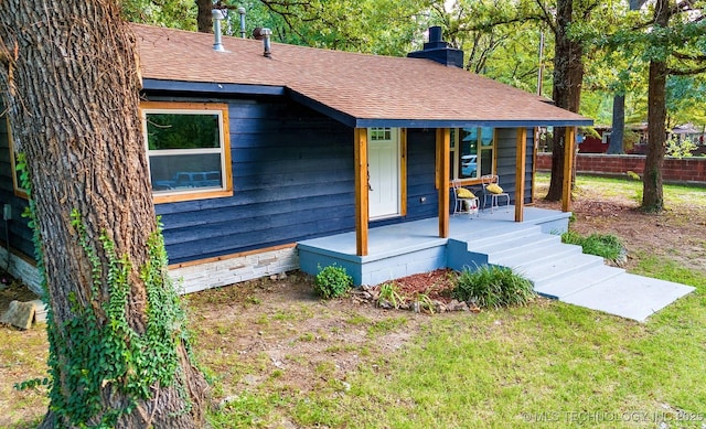 exterior space featuring a porch, a shingled roof, fence, a front lawn, and a chimney