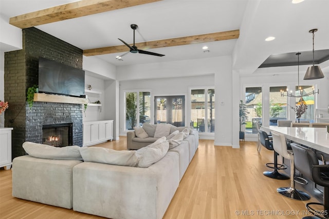 living area featuring plenty of natural light, beamed ceiling, a fireplace, and light wood-style floors