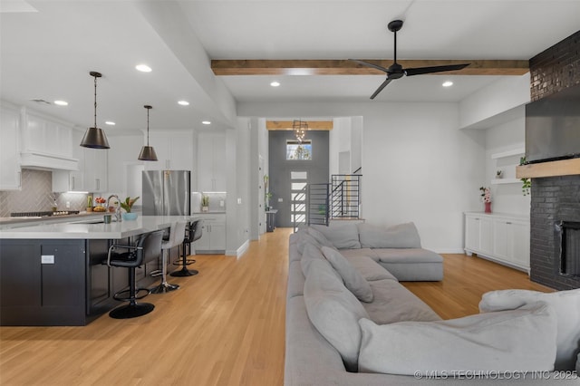 living room with baseboards, light wood-style flooring, stairs, a fireplace, and beam ceiling