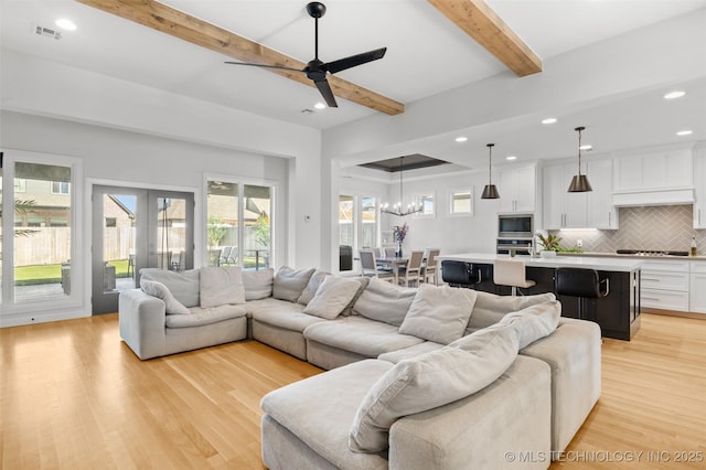 living area featuring light wood finished floors, beamed ceiling, visible vents, and a healthy amount of sunlight