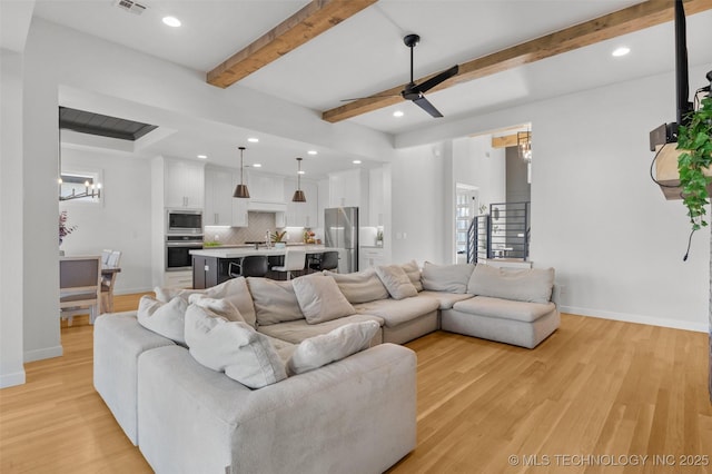 living room with light wood-style floors, ceiling fan with notable chandelier, beam ceiling, and stairs