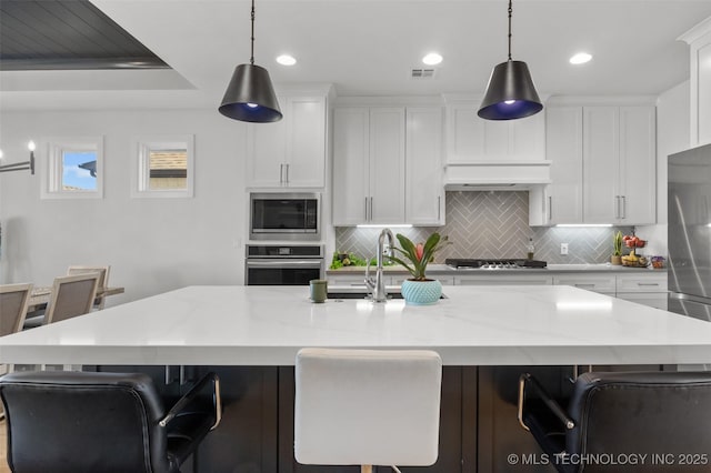 kitchen featuring stainless steel appliances, pendant lighting, a kitchen island with sink, and white cabinets