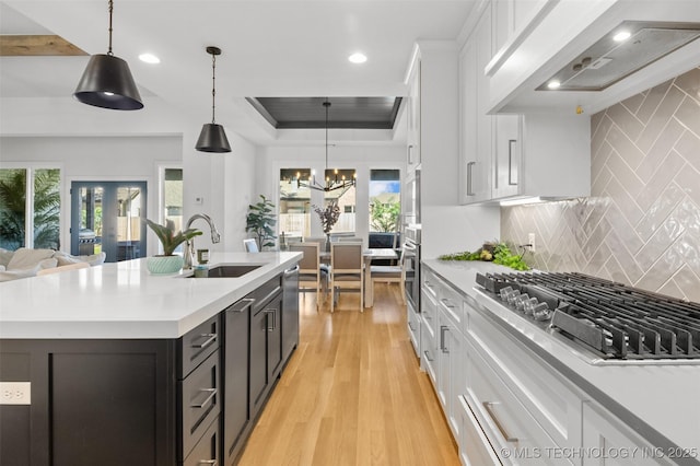 kitchen with decorative light fixtures, white cabinets, a center island with sink, and premium range hood