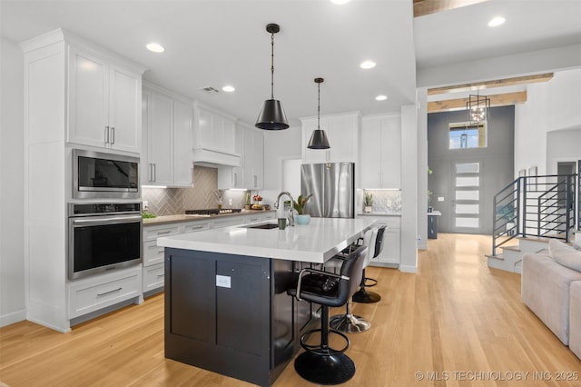 kitchen with a center island with sink, stainless steel appliances, light countertops, white cabinetry, and a sink