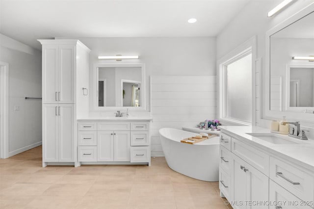 bathroom featuring two vanities, a sink, a freestanding bath, and tile patterned floors