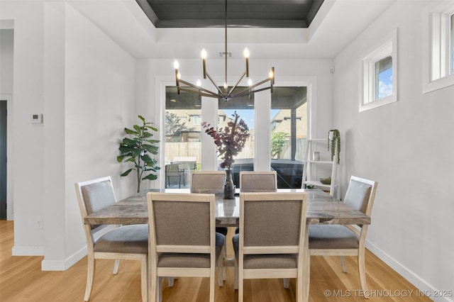 dining space featuring light wood-style floors, baseboards, a raised ceiling, and a chandelier