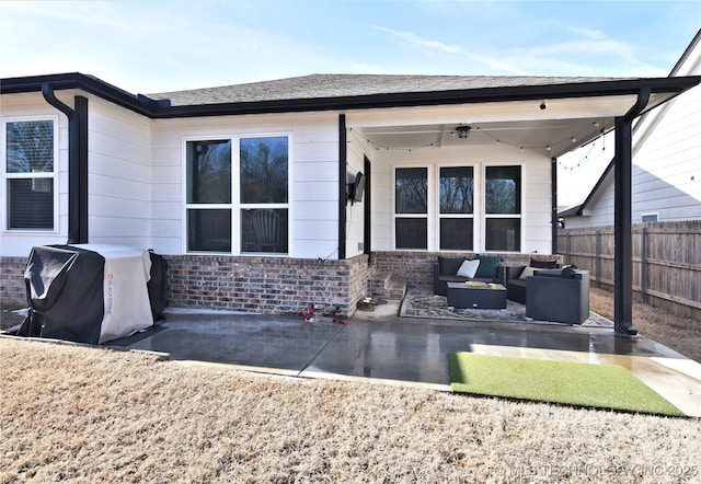 rear view of property featuring brick siding, a patio, a shingled roof, an outdoor hangout area, and fence