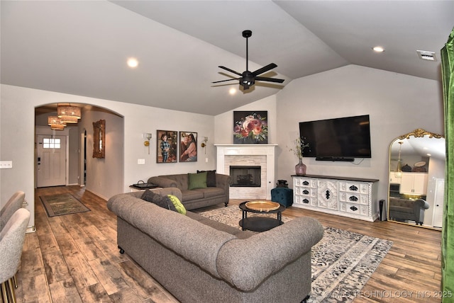 living area with arched walkways, ceiling fan, wood finished floors, vaulted ceiling, and a fireplace