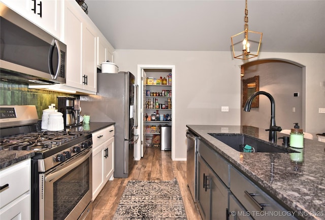 kitchen with pendant lighting, stainless steel appliances, white cabinets, a sink, and dark stone counters