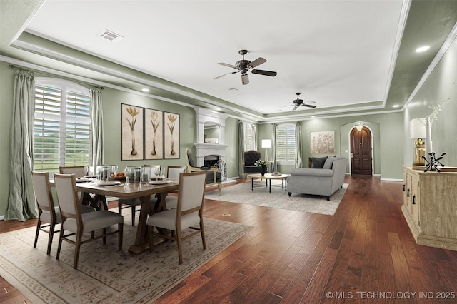 dining space featuring visible vents, a fireplace, arched walkways, and a raised ceiling