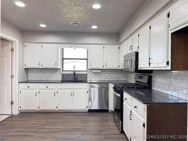 kitchen with appliances with stainless steel finishes, dark countertops, white cabinetry, and visible vents