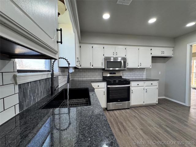 kitchen with appliances with stainless steel finishes, white cabinets, a sink, wood finished floors, and baseboards