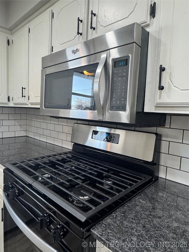 kitchen with gas range oven, stainless steel microwave, dark countertops, and white cabinets