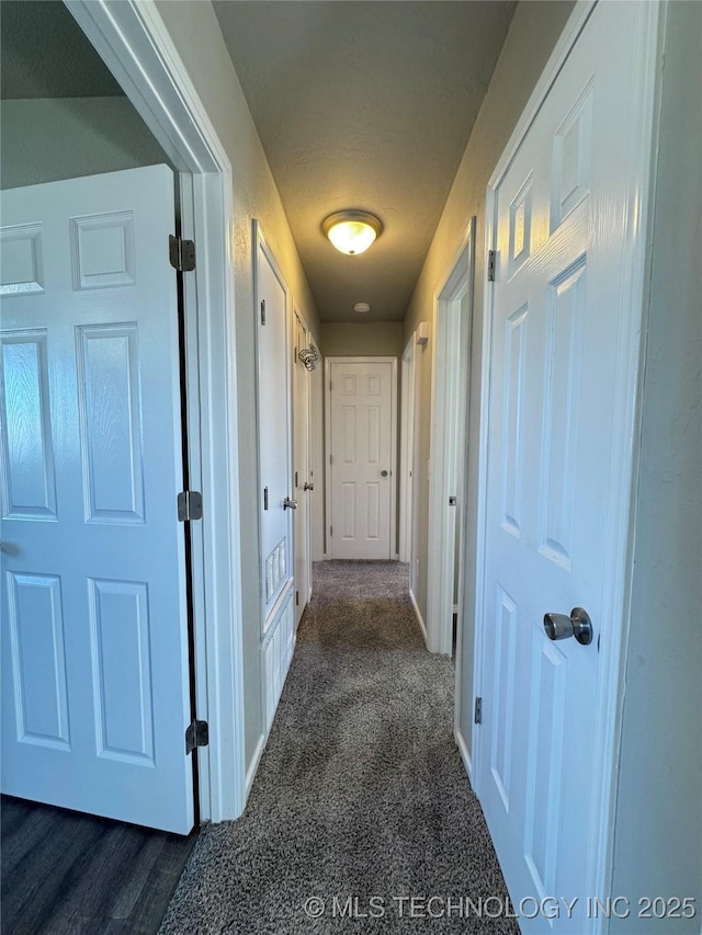 hall featuring baseboards and dark carpet