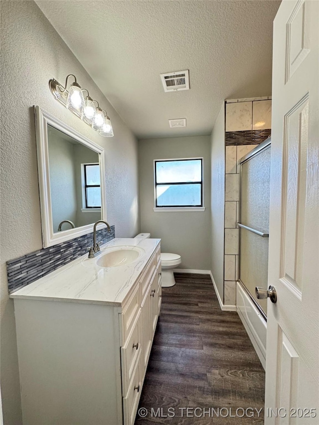 bathroom featuring enclosed tub / shower combo, a textured ceiling, wood finished floors, vanity, and visible vents