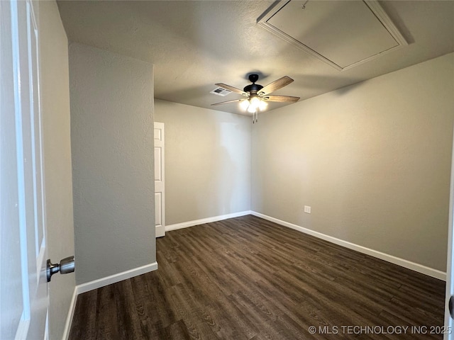 empty room featuring attic access, dark wood-style flooring, visible vents, and baseboards