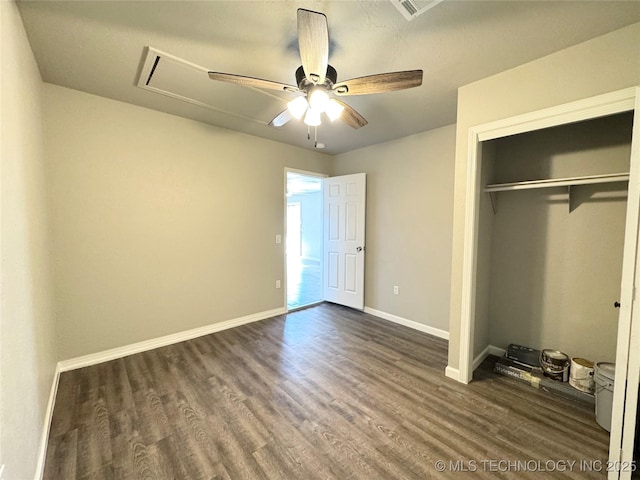 unfurnished bedroom with dark wood-style floors, a closet, attic access, and baseboards