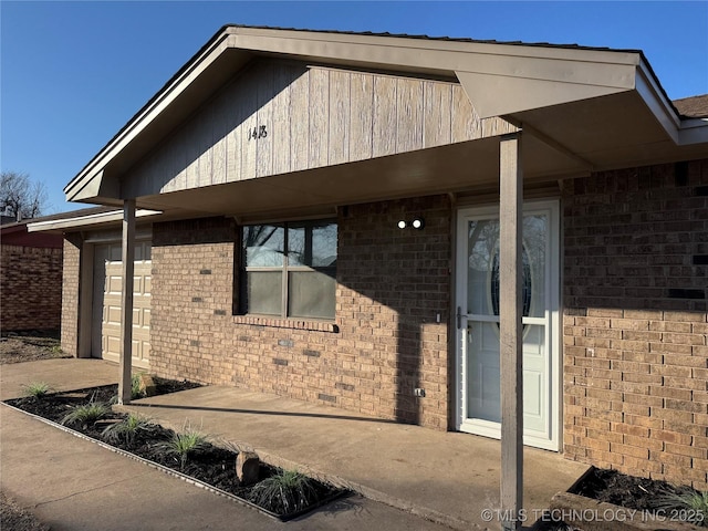 view of exterior entry featuring a garage, driveway, and brick siding