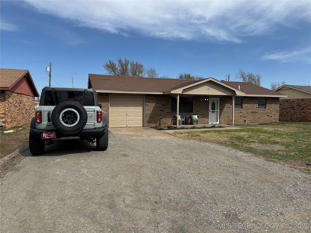 single story home with covered porch, brick siding, a garage, and driveway