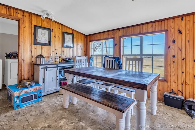 dining area featuring vaulted ceiling, washer / clothes dryer, and wooden walls