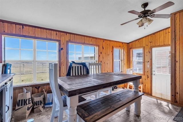 dining space with vaulted ceiling, ceiling fan, and wood walls