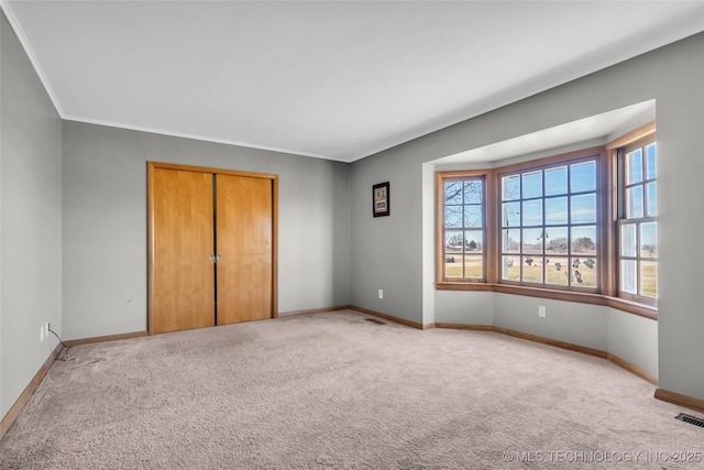 unfurnished bedroom featuring visible vents, baseboards, light colored carpet, ornamental molding, and a closet