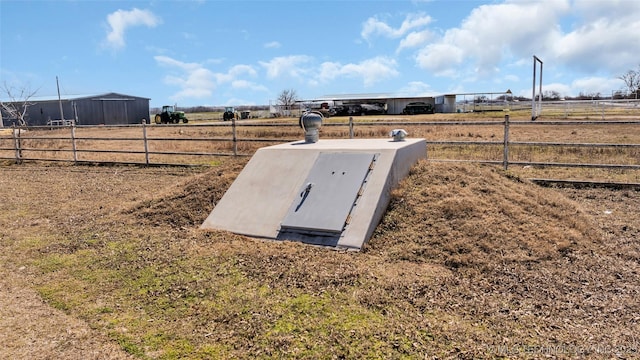 entry to storm shelter with a rural view and fence