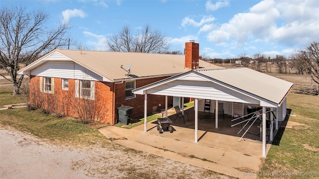 rear view of property featuring metal roof, driveway, brick siding, and a chimney