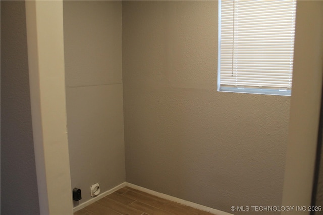 clothes washing area featuring wood finish floors, baseboards, laundry area, and a textured wall