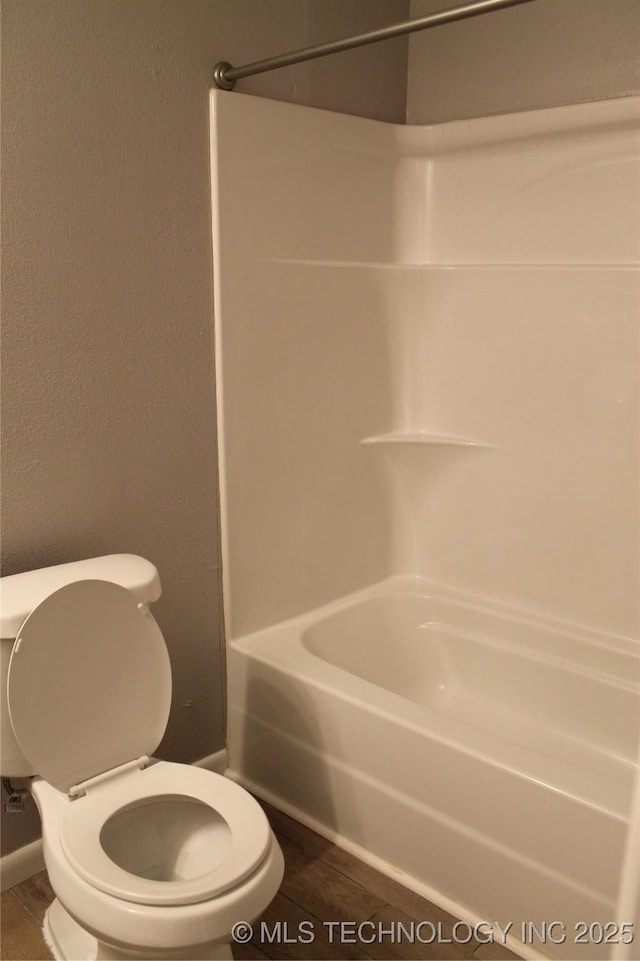 bathroom featuring tub / shower combination, toilet, and a textured wall