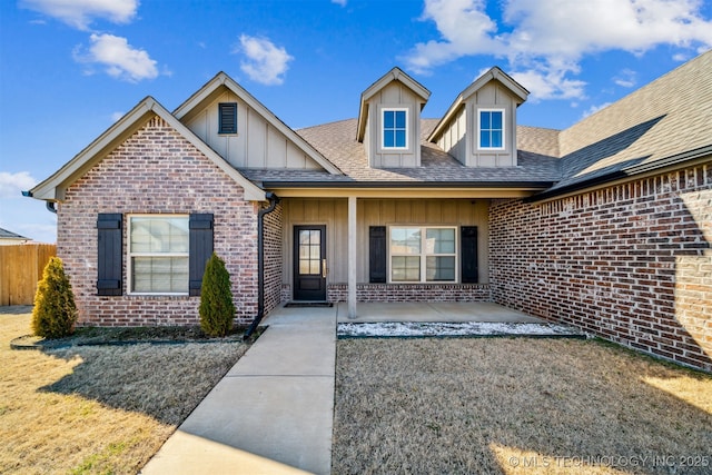 view of front of property featuring brick siding, a shingled roof, fence, board and batten siding, and a patio area