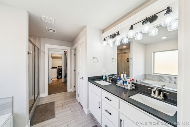 bathroom featuring a stall shower, visible vents, a walk in closet, and a sink