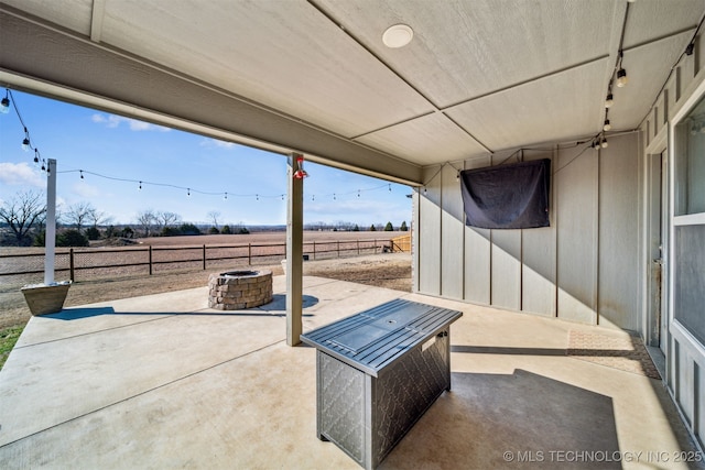 view of patio with an outdoor fire pit, a rural view, and fence