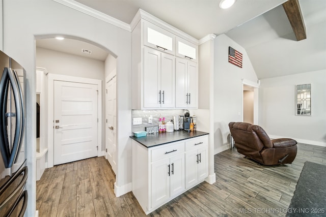 kitchen with glass insert cabinets, dark countertops, stainless steel refrigerator, and white cabinetry