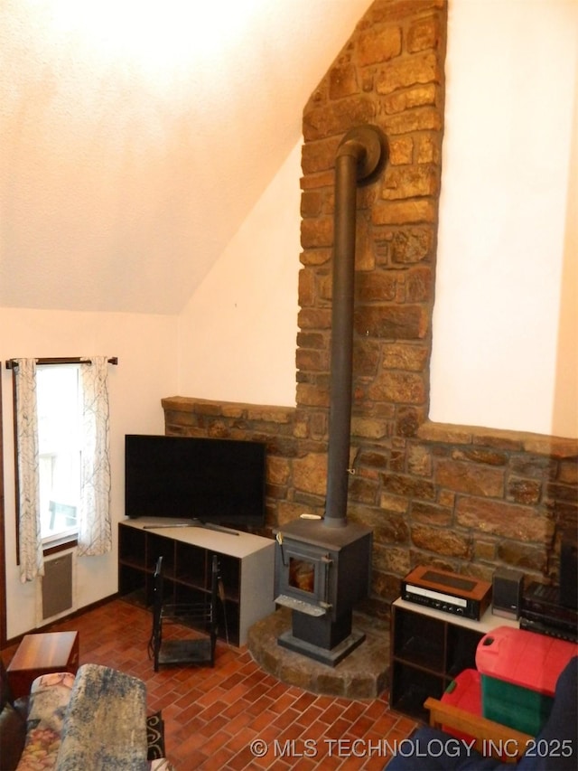 living room featuring a wood stove, brick floor, and lofted ceiling