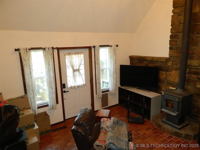 living area with lofted ceiling, a wood stove, visible vents, and brick floor