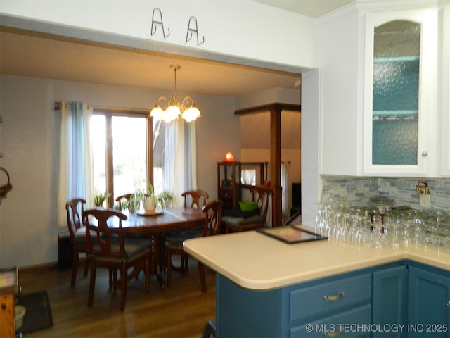 kitchen featuring glass insert cabinets, white cabinets, light countertops, tasteful backsplash, and decorative light fixtures