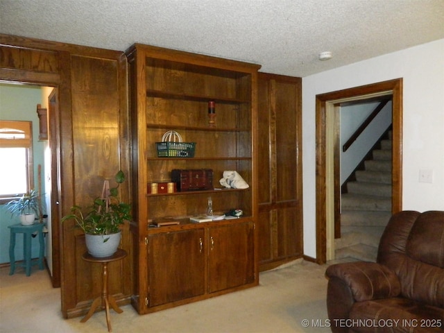sitting room featuring light carpet, a textured ceiling, and stairs
