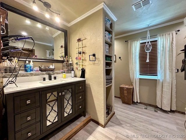 bathroom featuring wood finished floors, ornamental molding, vanity, and visible vents