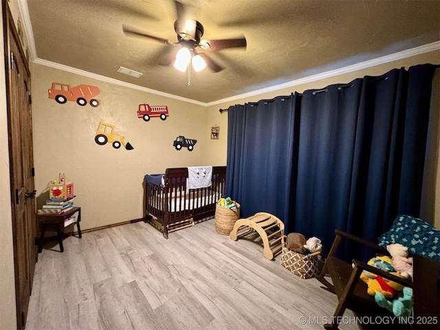 bedroom featuring a crib, visible vents, ornamental molding, and wood finished floors