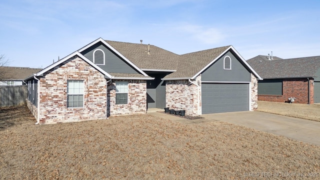 view of front facade with fence, driveway, roof with shingles, a garage, and brick siding