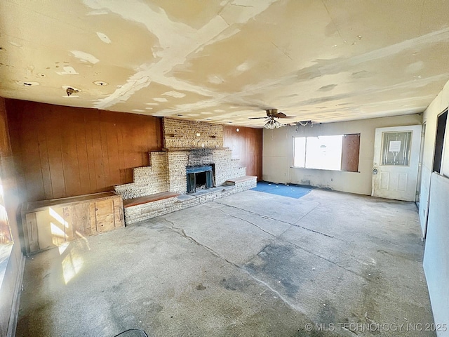 unfurnished living room featuring a fireplace, wooden walls, and ceiling fan