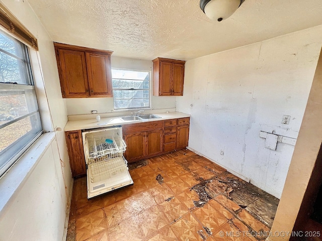 kitchen featuring a textured ceiling, a sink, light countertops, dishwasher, and brown cabinetry