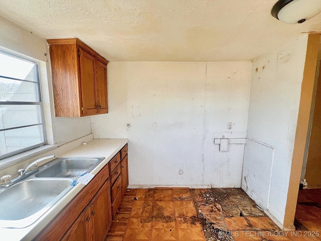 kitchen with a sink, a textured ceiling, brown cabinets, and light countertops