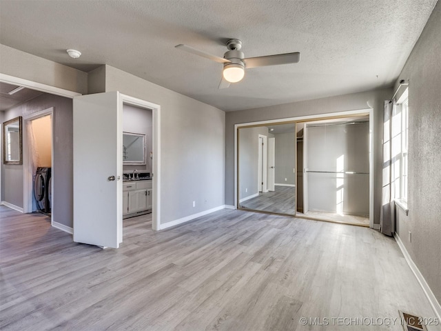 unfurnished bedroom with a textured ceiling, baseboards, light wood-style floors, washer and dryer, and a closet