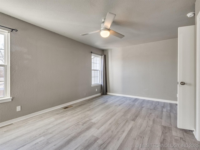 unfurnished room with light wood-style floors, visible vents, baseboards, and a ceiling fan