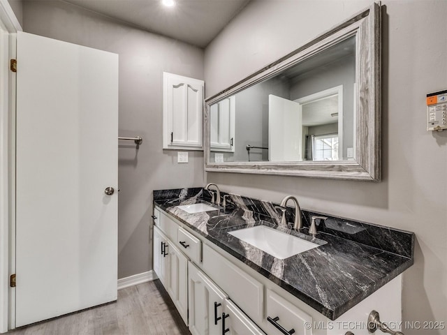 full bathroom featuring double vanity, a sink, baseboards, and wood finished floors